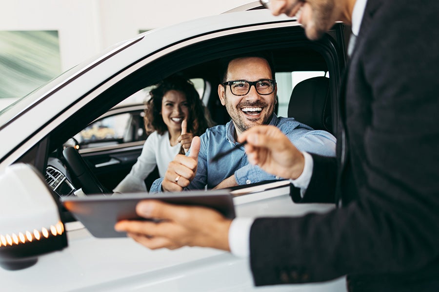 Couple sitting in a car in a car dealership next to a salesperson